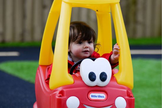 This image shows toddler playing in a push along toy car