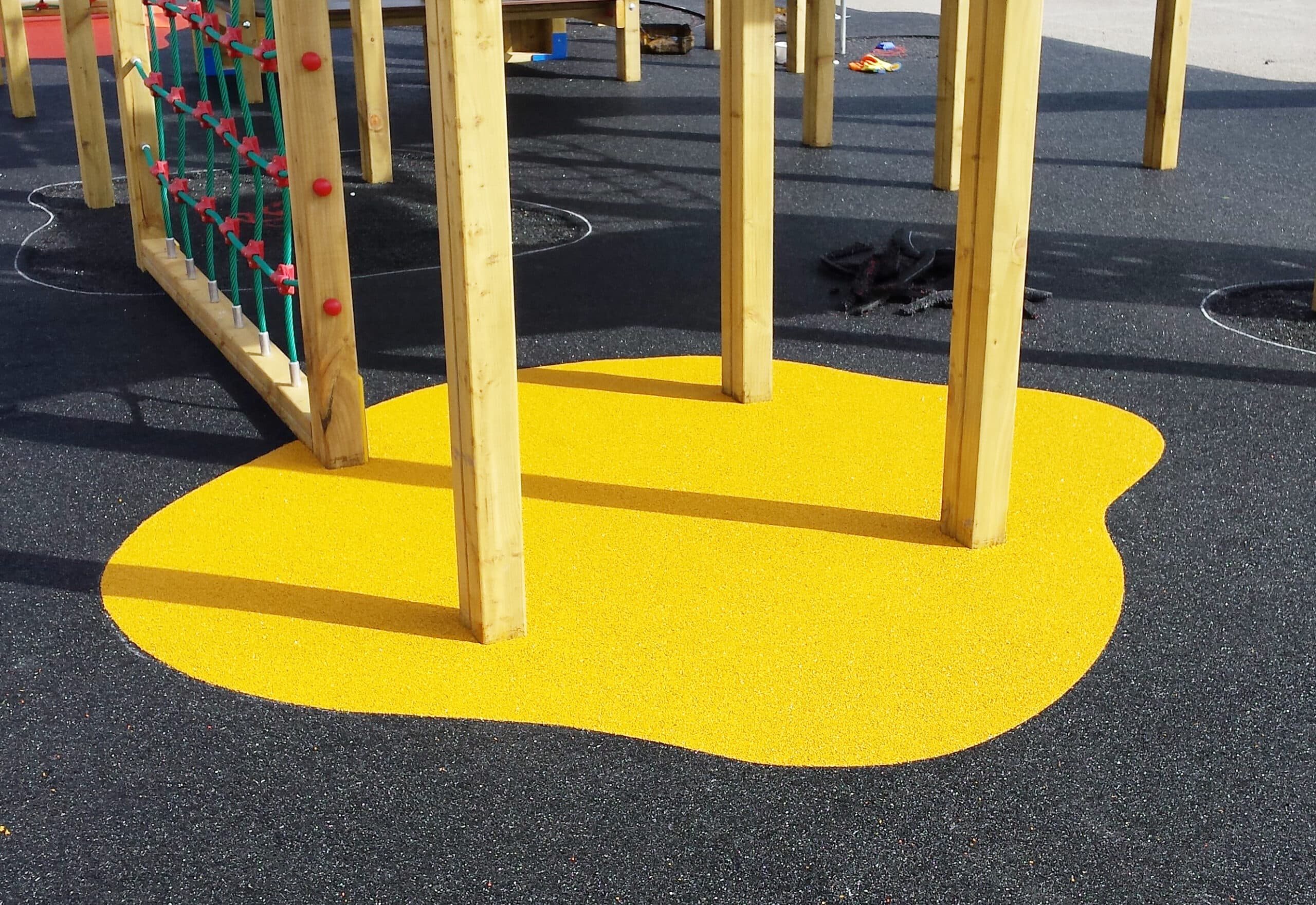 Yellow wetpour surfacing surrounding wooden posts buried in the ground, but atop black surfacing
