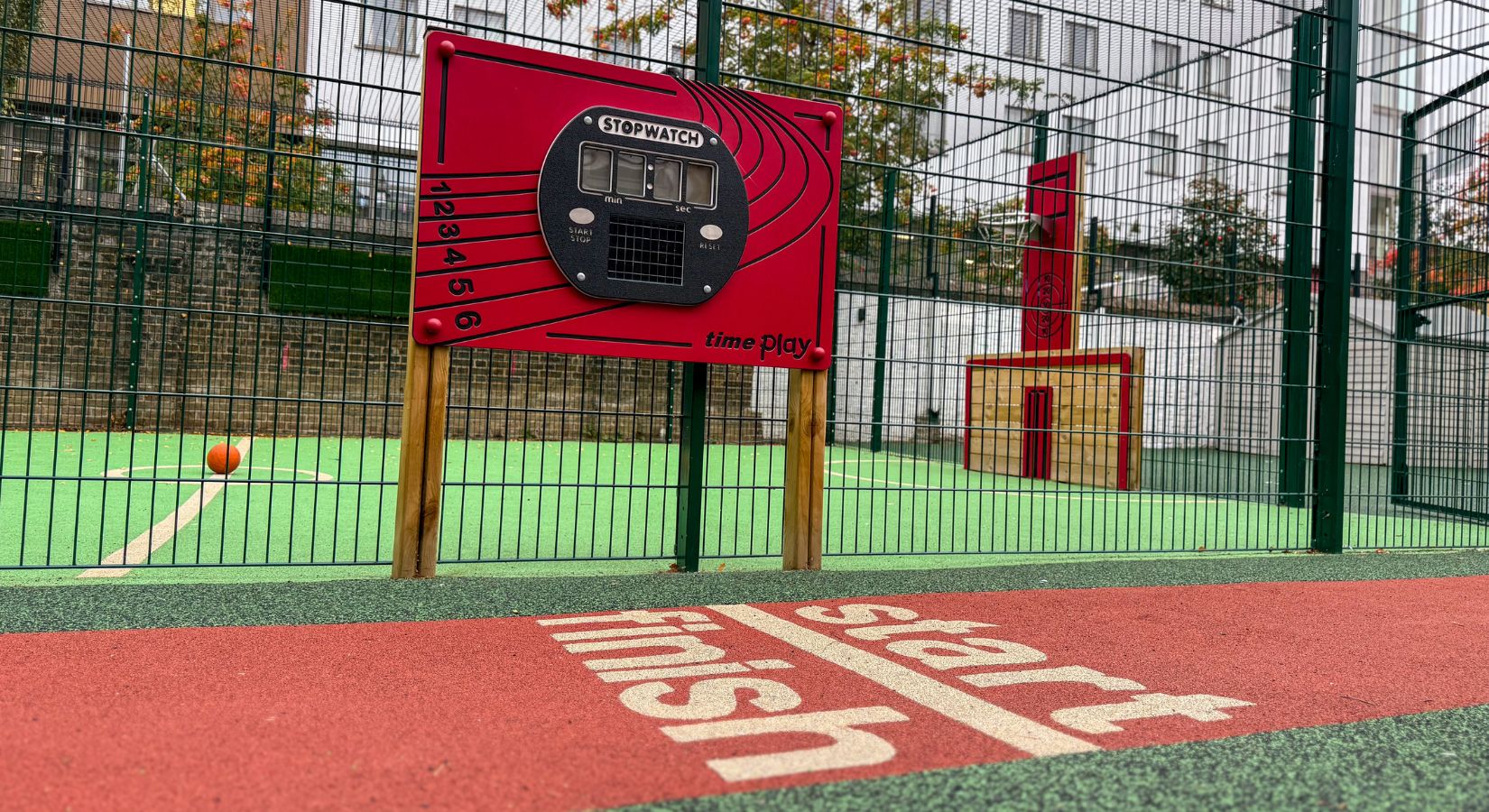 Red playboard featuring a stopwatch dominating a section of red running track at a school
