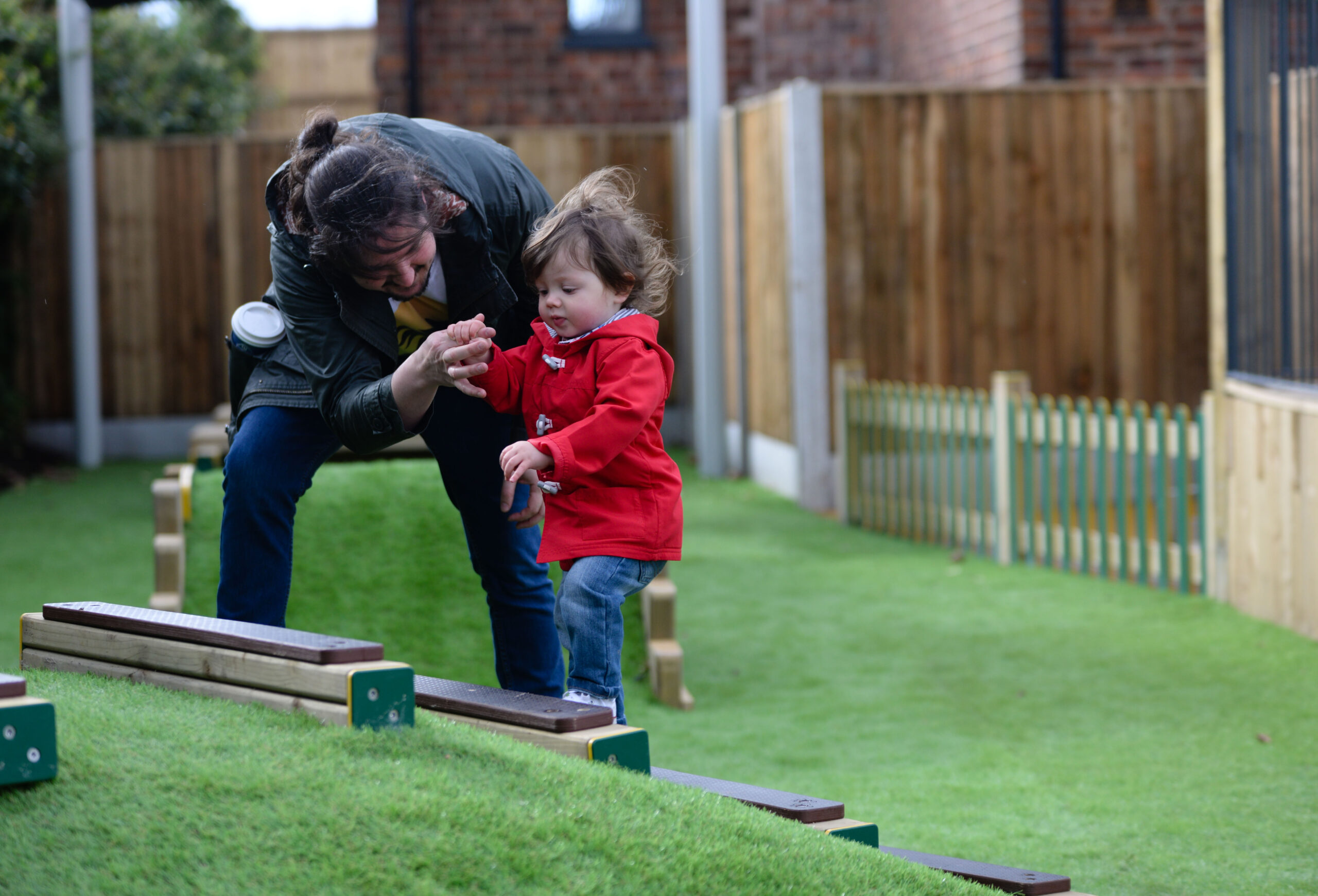 A woman helps a small girl in a red coat up some steps at a playground