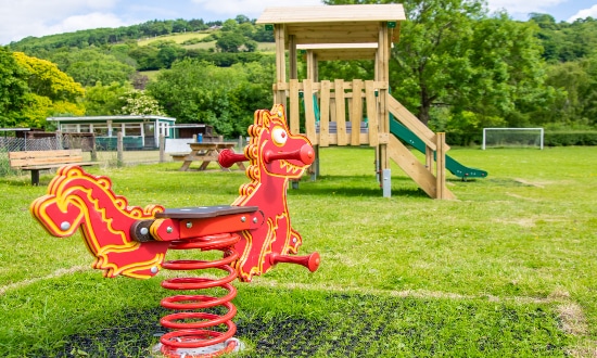 Red dragon playground springer in foreground with a wooden tower in the background