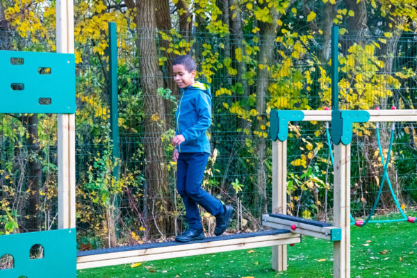A boy walks along a trim trail balance beam