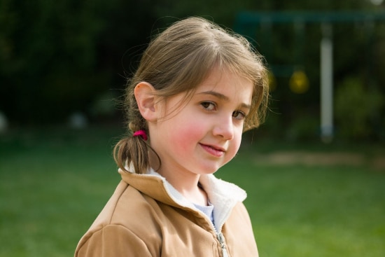 Little brown-haired girl with a wry smile to camera