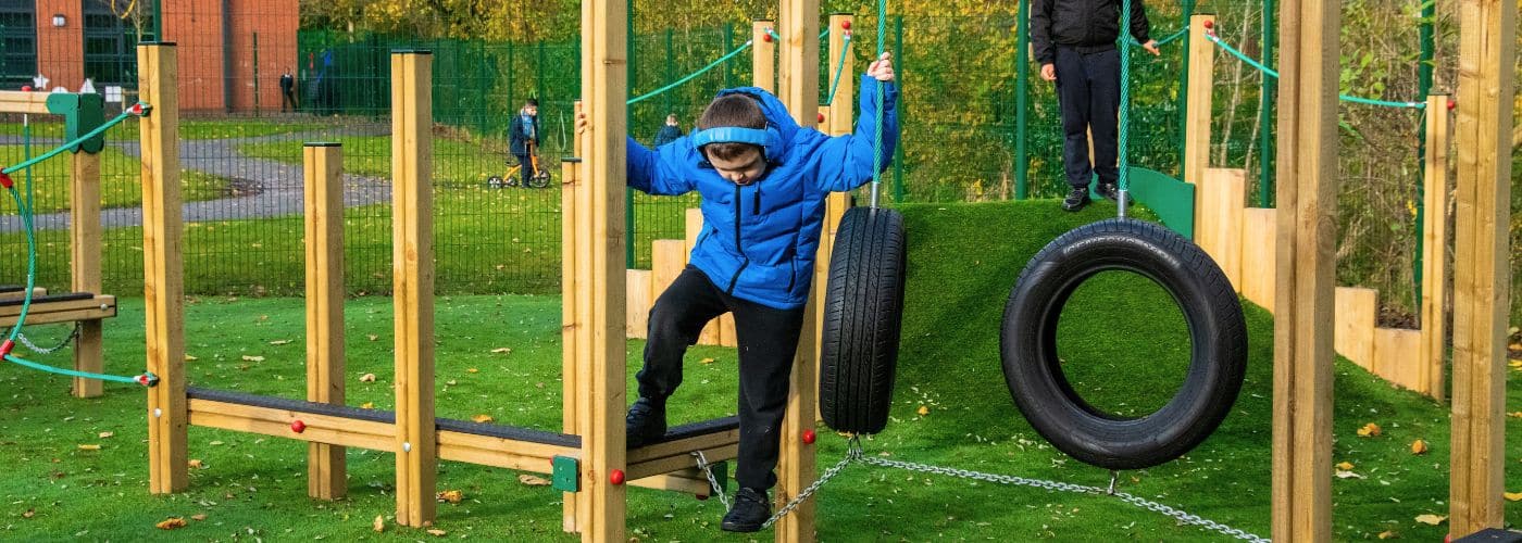 Child holding on to a tyre swing while navigating a chain bridge
