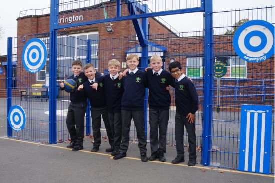 This image shows several young boys in school uniform standing in front of a MUGA
