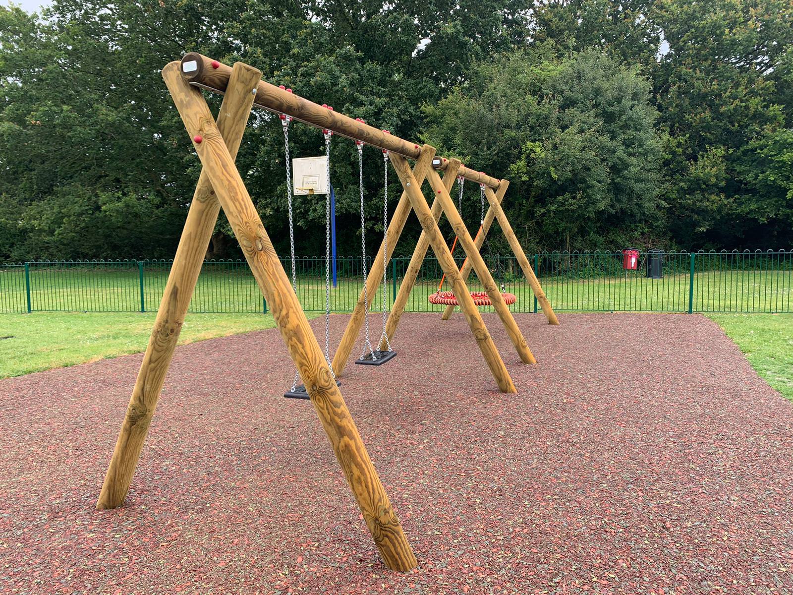 Round timber swing structure installed on a red black fleck rubber mulch surface