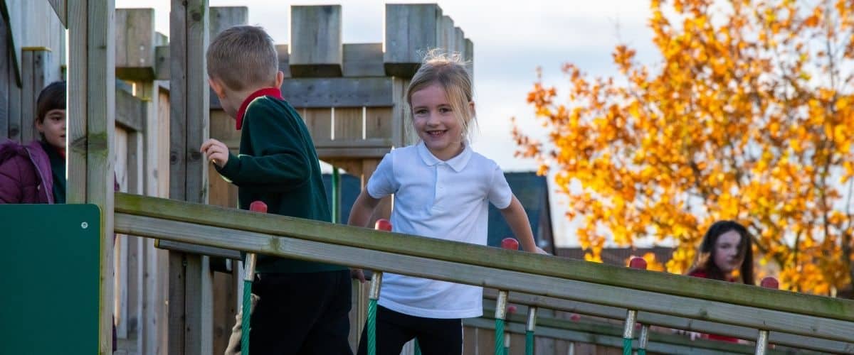 This image shows two primary school pupils playing on a wooden castle piece of playground equipment