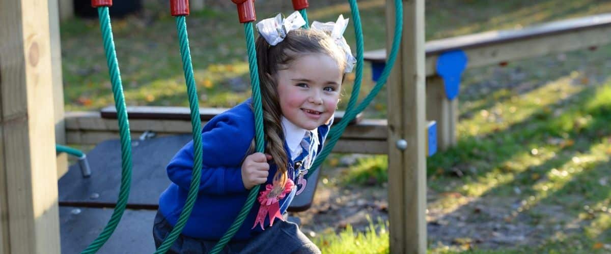 This image shows a young female primary pupil playing on a rope bridge piece of playground equipment