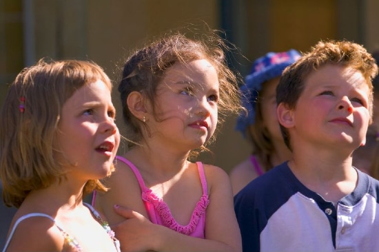 children sat outside paying attention to someone off-camera