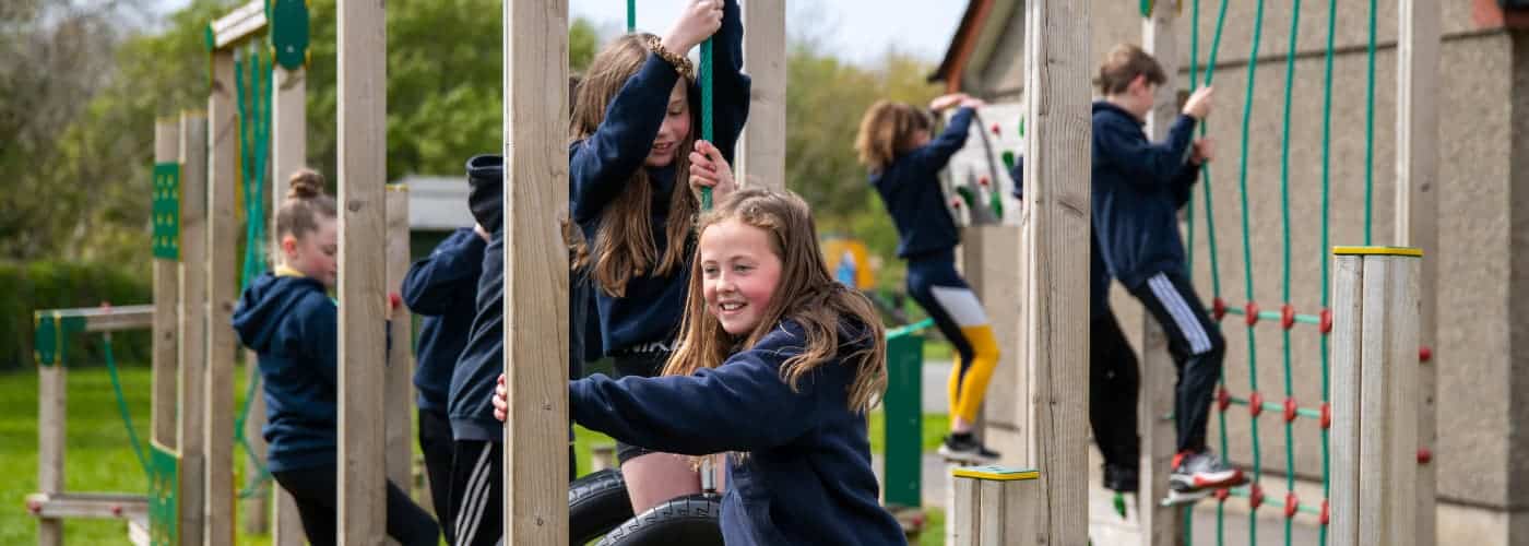 Several school children playing on an adventure trail, a girl in the foreground smiling