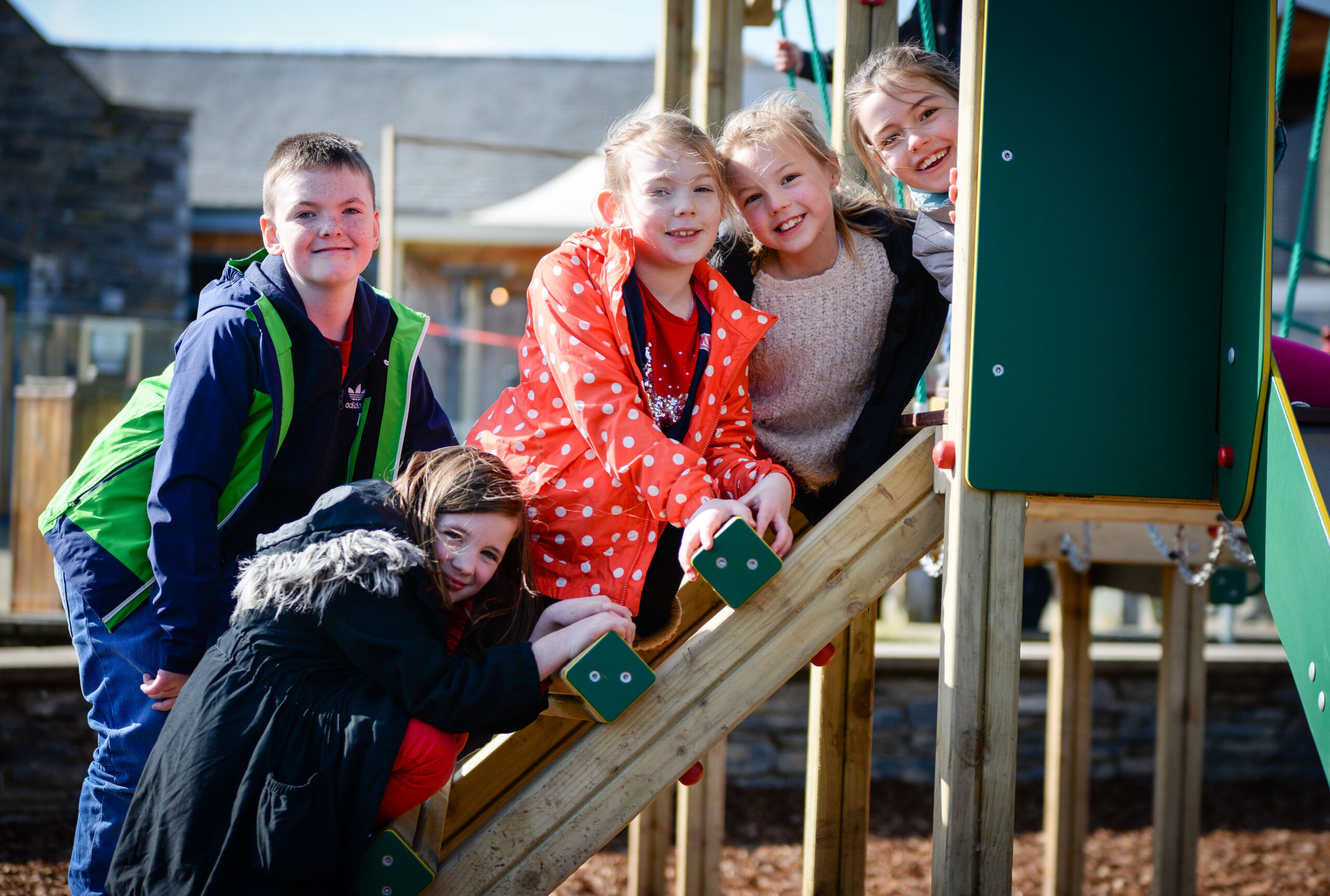 5 children of varying genders pose for a photo while sat on a slide at the playground