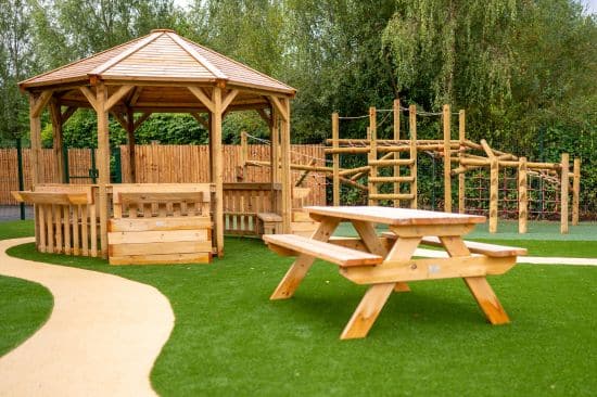 This image shows a Octavia shelter, picnic bench and a combi jungle climber on both wetpour safety surfacing and artificial grass safety surfacing