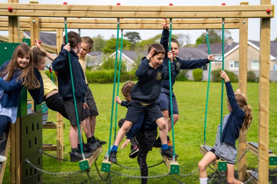 This image shows several school children climbing and swinging from a rope bridge 