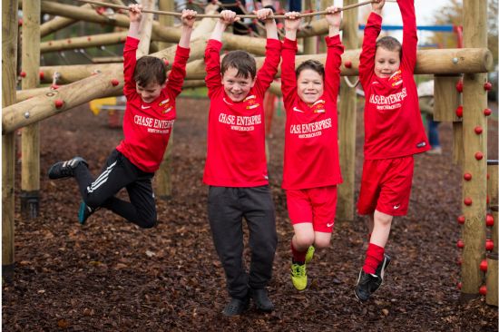 This image shows four young boys in sports kits swinging off a rope