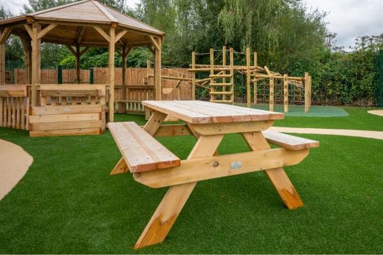 This image shows a Octavia shelter, picnic bench and a combi jungle climber on both wetpour safety surfacing and artificial grass safety surfacing