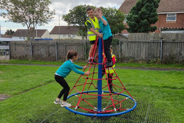 This image shows children playing on a rope net pyramid spinner on grass