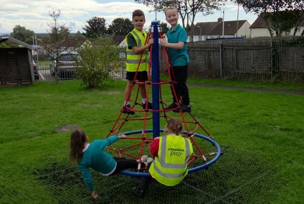 This image shows children playing on a rope net pyramid spinner on grass