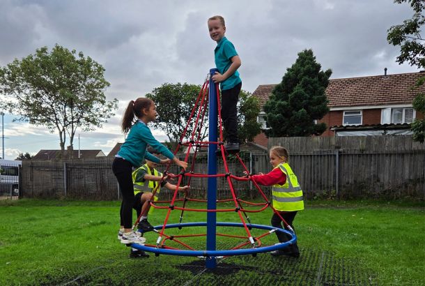 This image shows children playing on a rope net pyramid spinner on grass